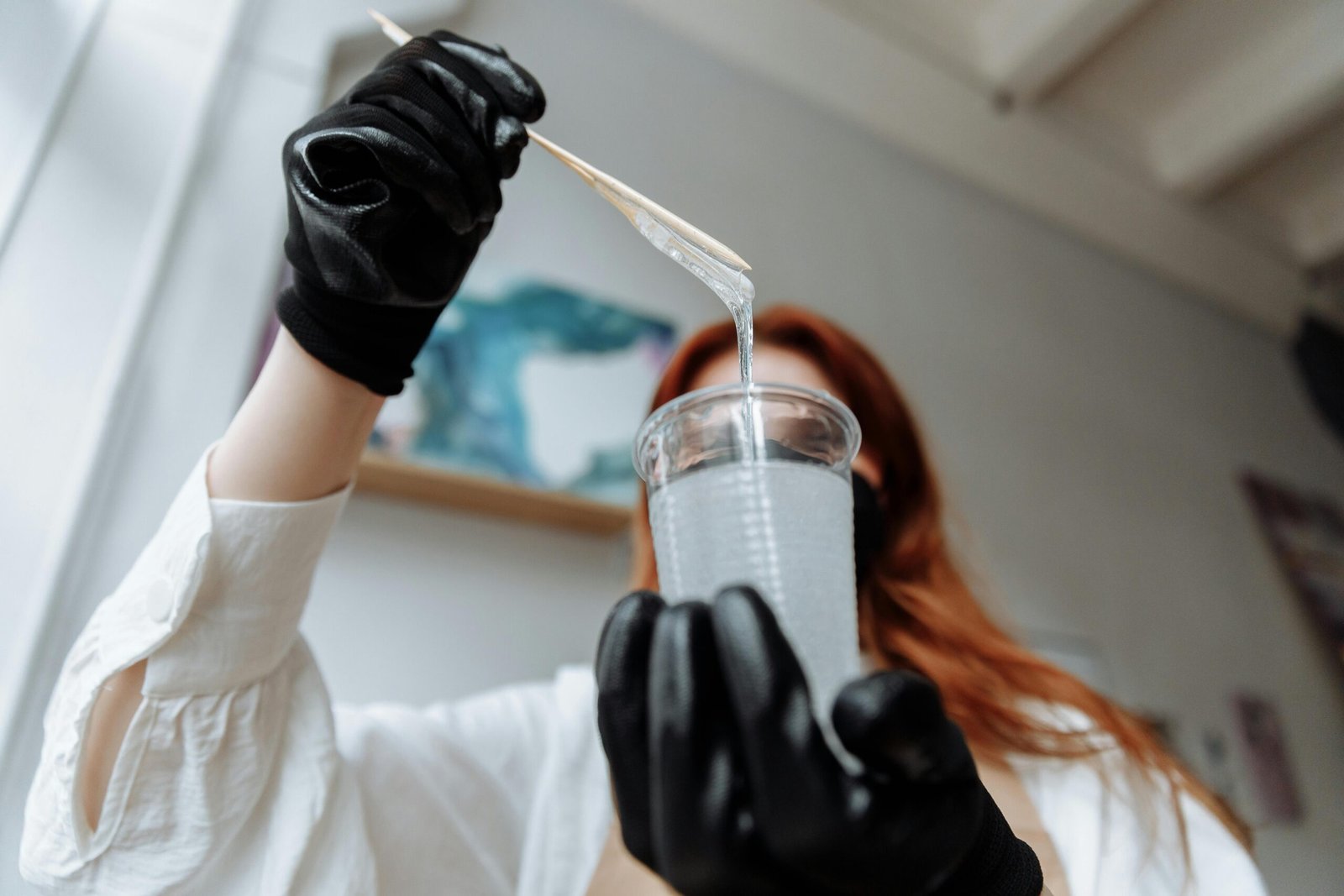 A person demonstrating resin mixing while wearing black gloves indoors with ambient light.
